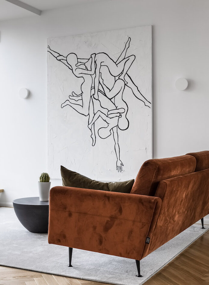 didelis grafinis paveikslas ir oranžinė aksominė sofa interjere